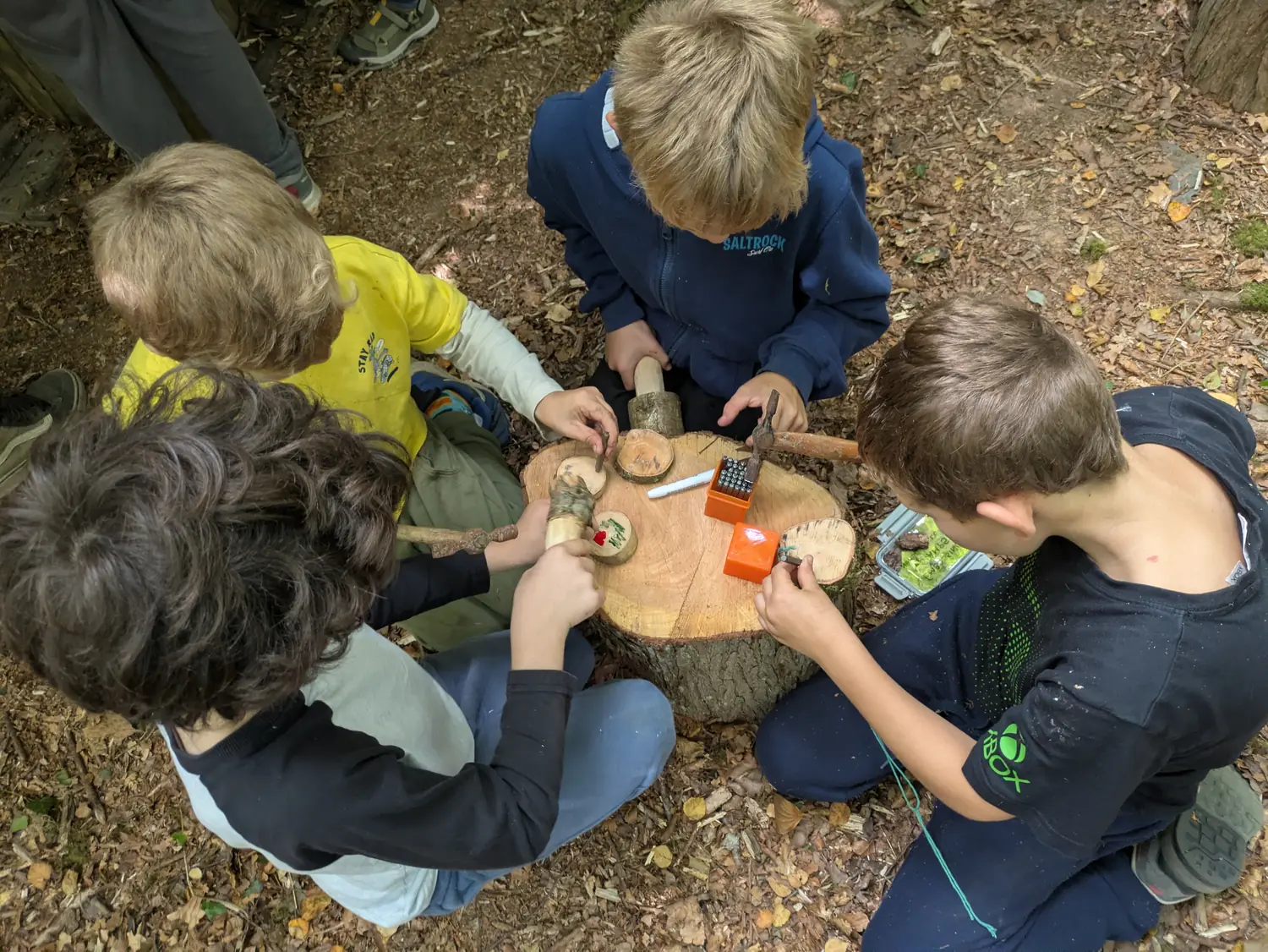 Four children sitting around a log stump, whittling and working with hand tools